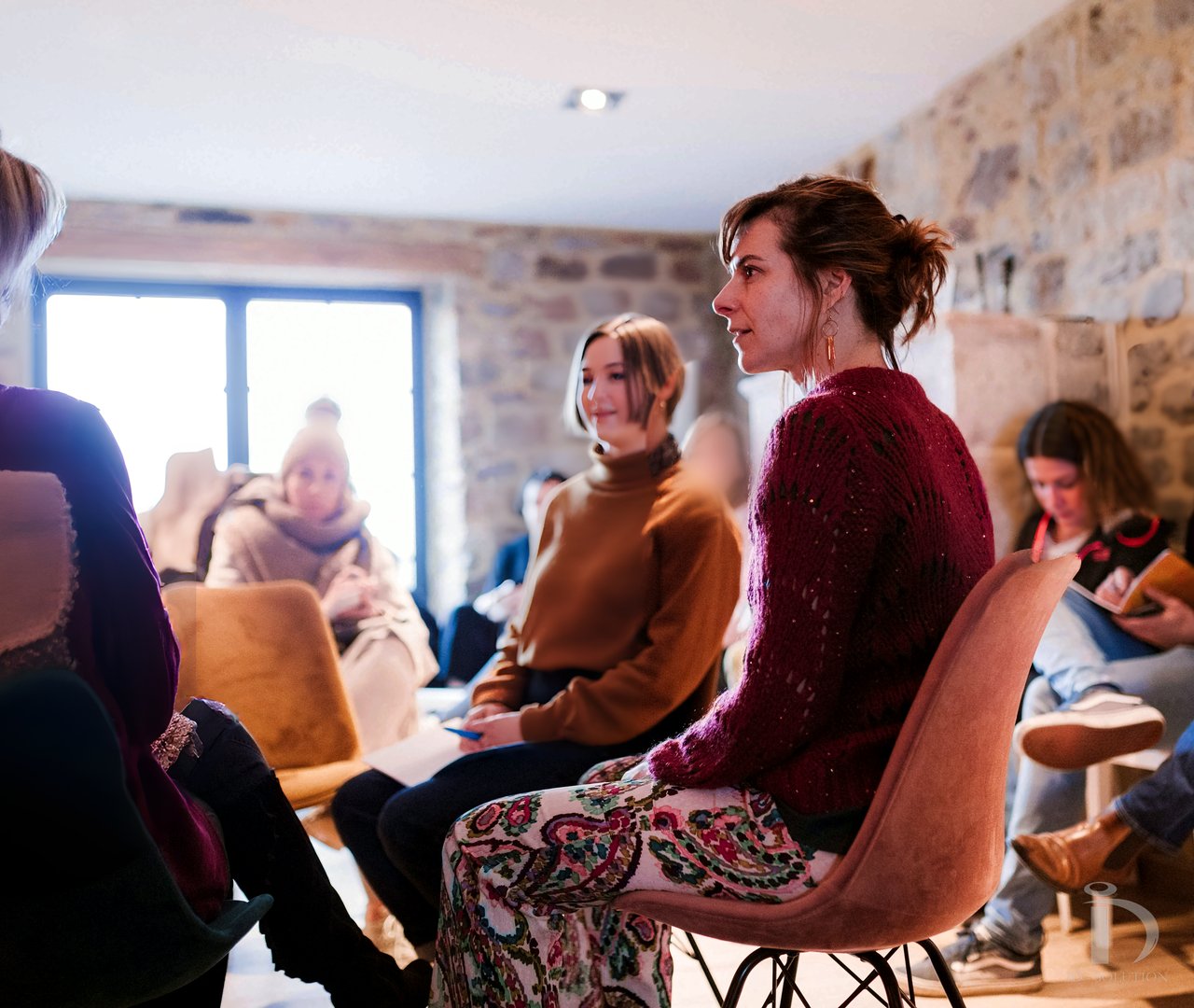 Aline Stukkens écoute un échange en atelier, dans une salle aux murs de pierre